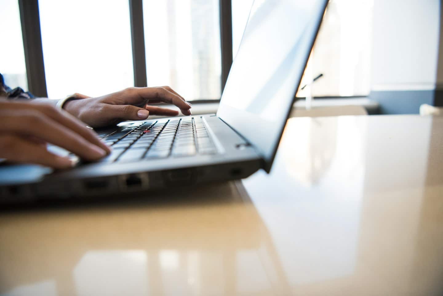 Dark-skinned hands typing on a laptop keyboard.